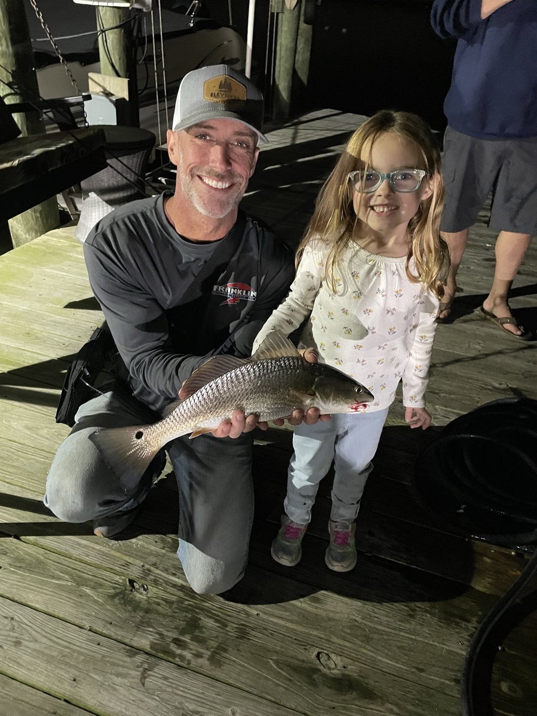 Two anglers holding a fish on the dock at night